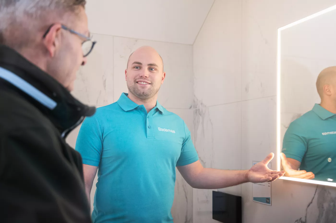 Mann viser frem speil på utstilling for bad og våtrom i butikk hos Gården Rørleggerservice AS